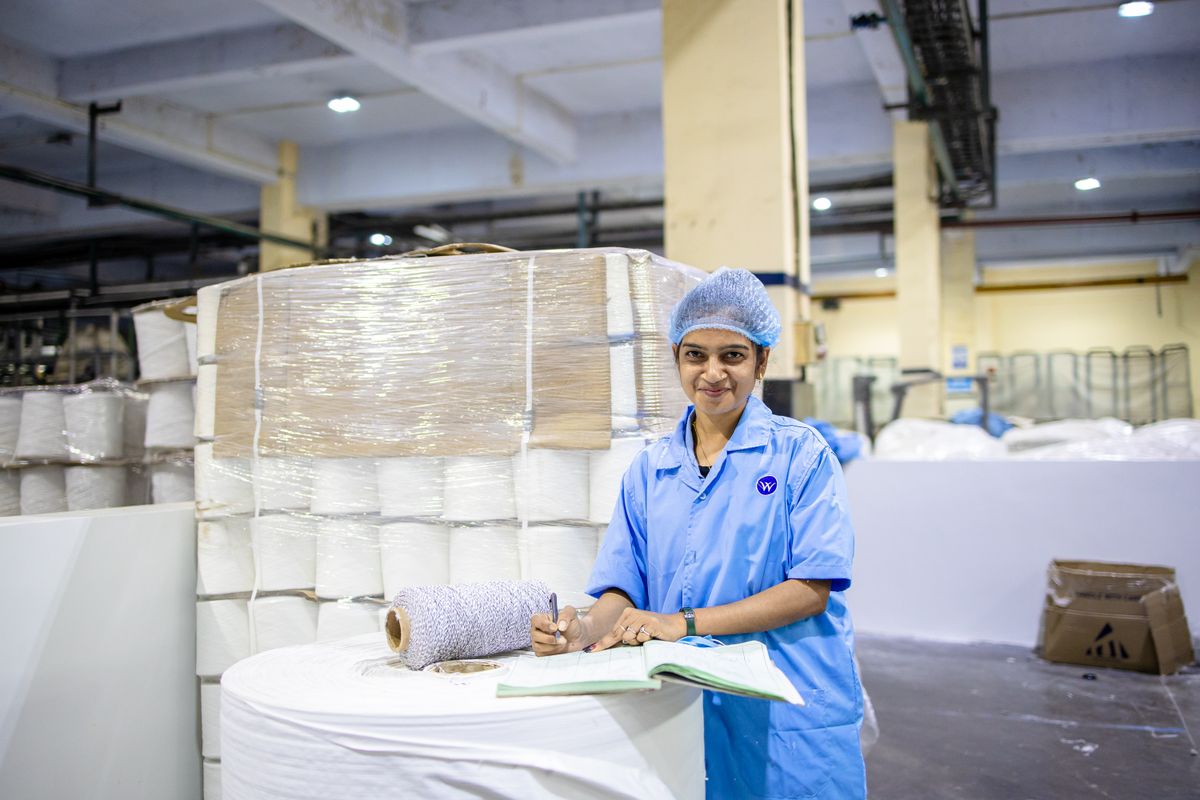 Smiling female textile worker taking notes in a factory with yarn stacks