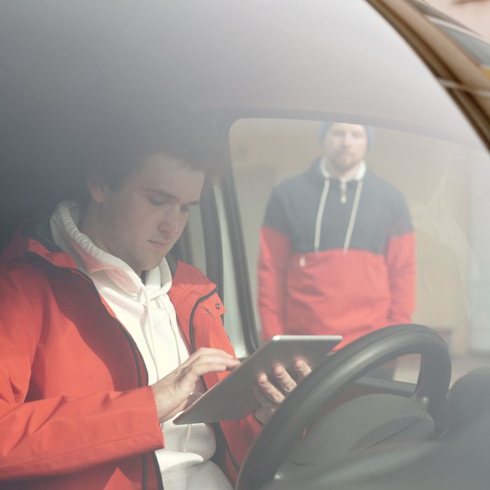 Young man in orange jacket using smartphone inside a car