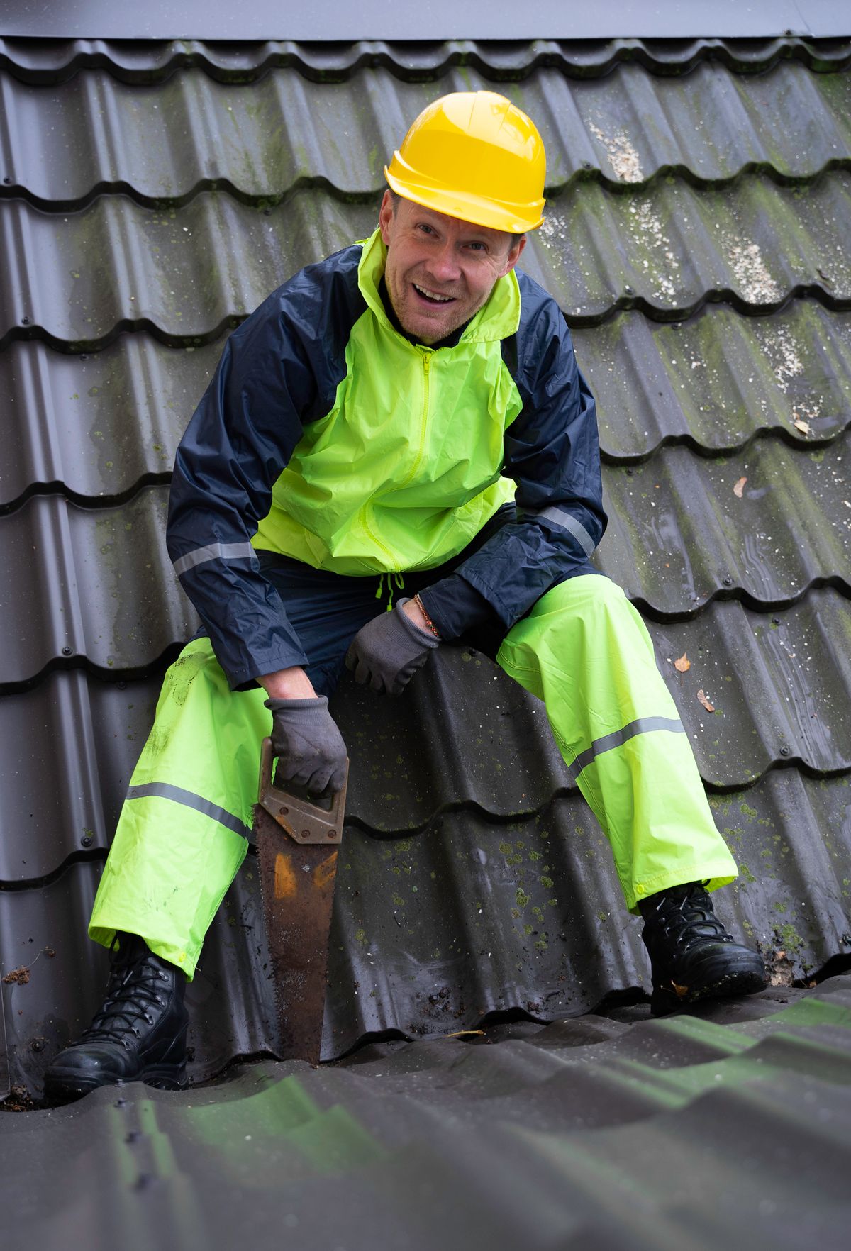 Smiling construction worker wearing safety gear cutting roof tiles with a saw